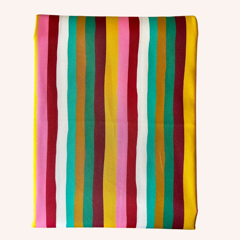A square fabric item, likely a napkin or small tablecloth, featuring a vibrant vertical stripe pattern with alternating bands of pink, white, teal green, burgundy, mustard yellow, and solid yellow, set against a plain off-white background.
