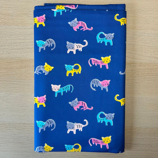 A folded piece of blue fabric with a repeating pattern of colorful cartoon cats in pink, yellow, blue, gray, and white, displayed flat on a light wood surface.