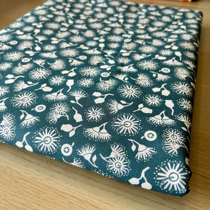 A folded piece of fabric with a dark teal blue background and a white repeating floral and abstract botanical pattern, displayed on a light wood surface.