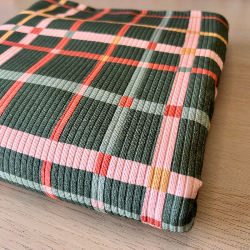 Ribbed Knit fabric featuring a multicolor plaid pattern with dark green, pink, orange, and light blue stripes, shown on a light wood surface.
