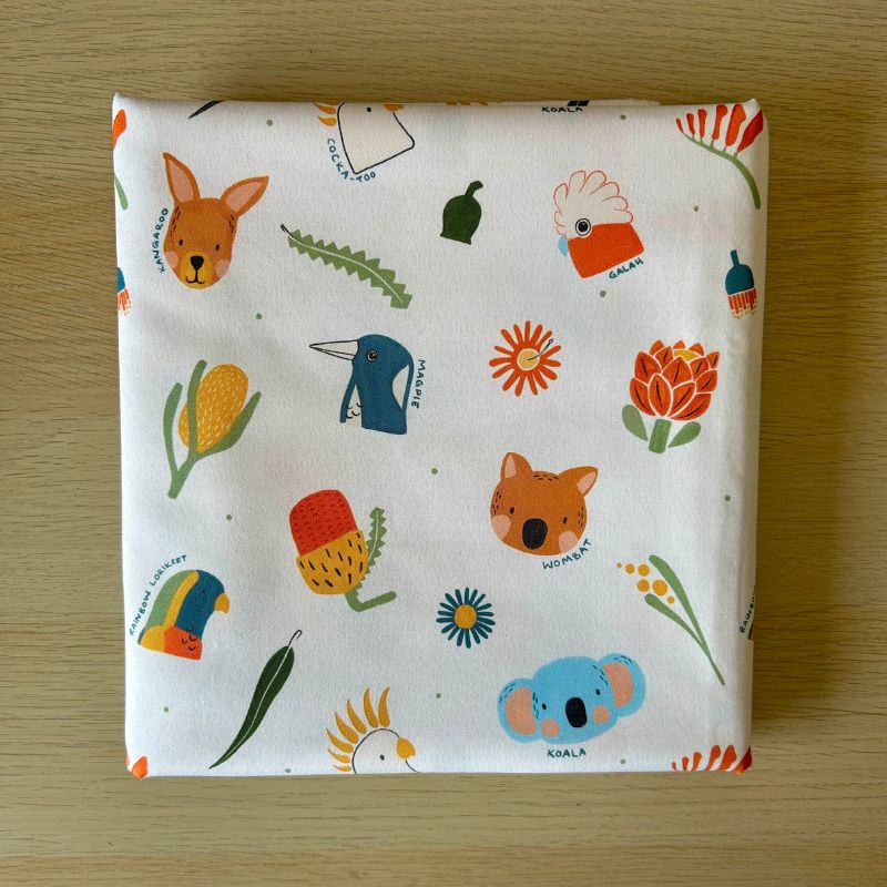 Cotton fabric featuring a colorful Australian-themed animal and nature print, displayed flat on a light wood surface.