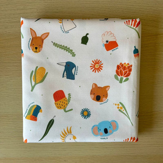Cotton fabric featuring a colorful Australian-themed animal and nature print, displayed flat on a light wood surface.