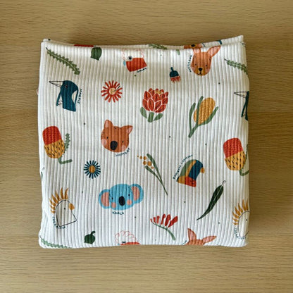 Ribbed fabric pouch with a colorful Australian-themed animal and flower print, laid flat on a light wood background.