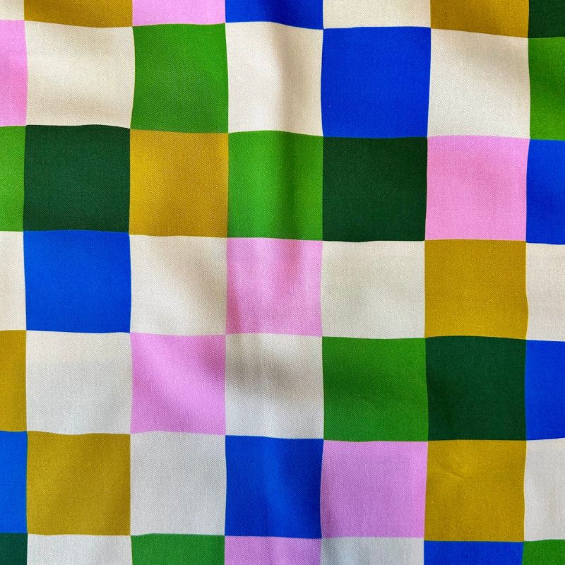 A close-up of a multicolor checkered fabric pattern with alternating squares in green, blue, pink, mustard yellow, dark green, and off-white.