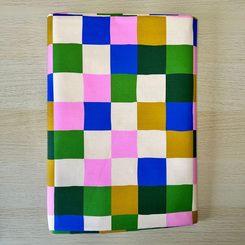 Canvas fabric with a colorful checkered pattern, lying flat on a light wood-grained surface.
