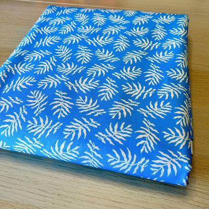 A folded piece of blue fabric with a repeating white palm leaf pattern, displayed on a light wood surface.