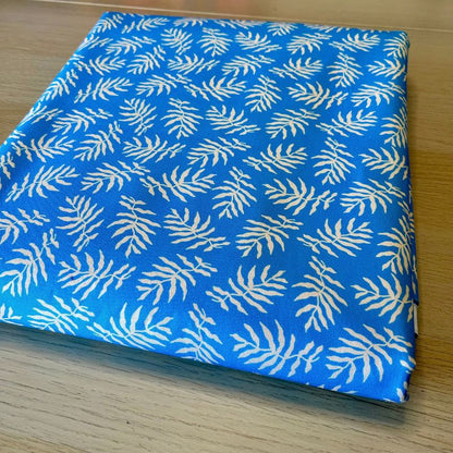 A folded piece of blue fabric with a repeating white palm leaf block print, displayed on a light wood surface.