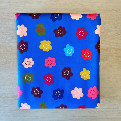 A square piece of blue fabric with a colorful floral pattern, laid flat on a light wood surface.