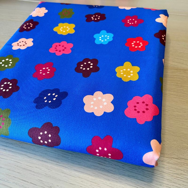 A folded piece of blue fabric with a colorful floral pattern, resting on a light wood surface.