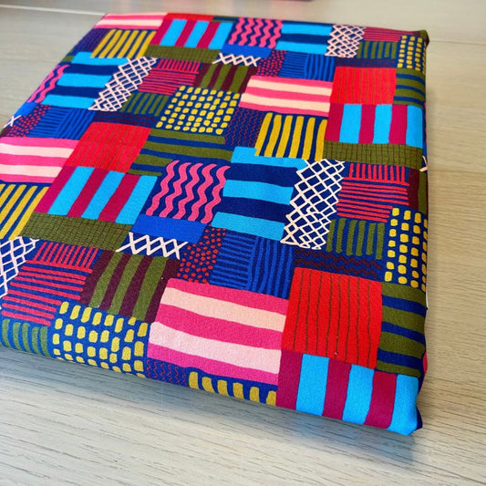 A folded piece of vibrant patchwork fabric with a multicolor geometric pattern, displayed on a light wood surface.
