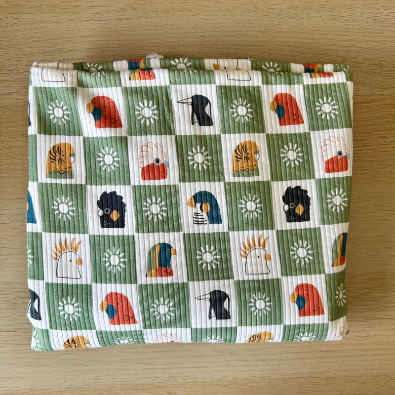A folded piece of green and white checkered fabric with a colorful bird pattern, displayed flat on a light wood surface.