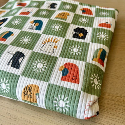 Green and white checkered pattern fabric with colorful cartoon birds, suns, and animals on a light wood background.